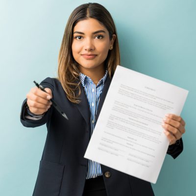 Confident young female professional with contract and pen against colored background